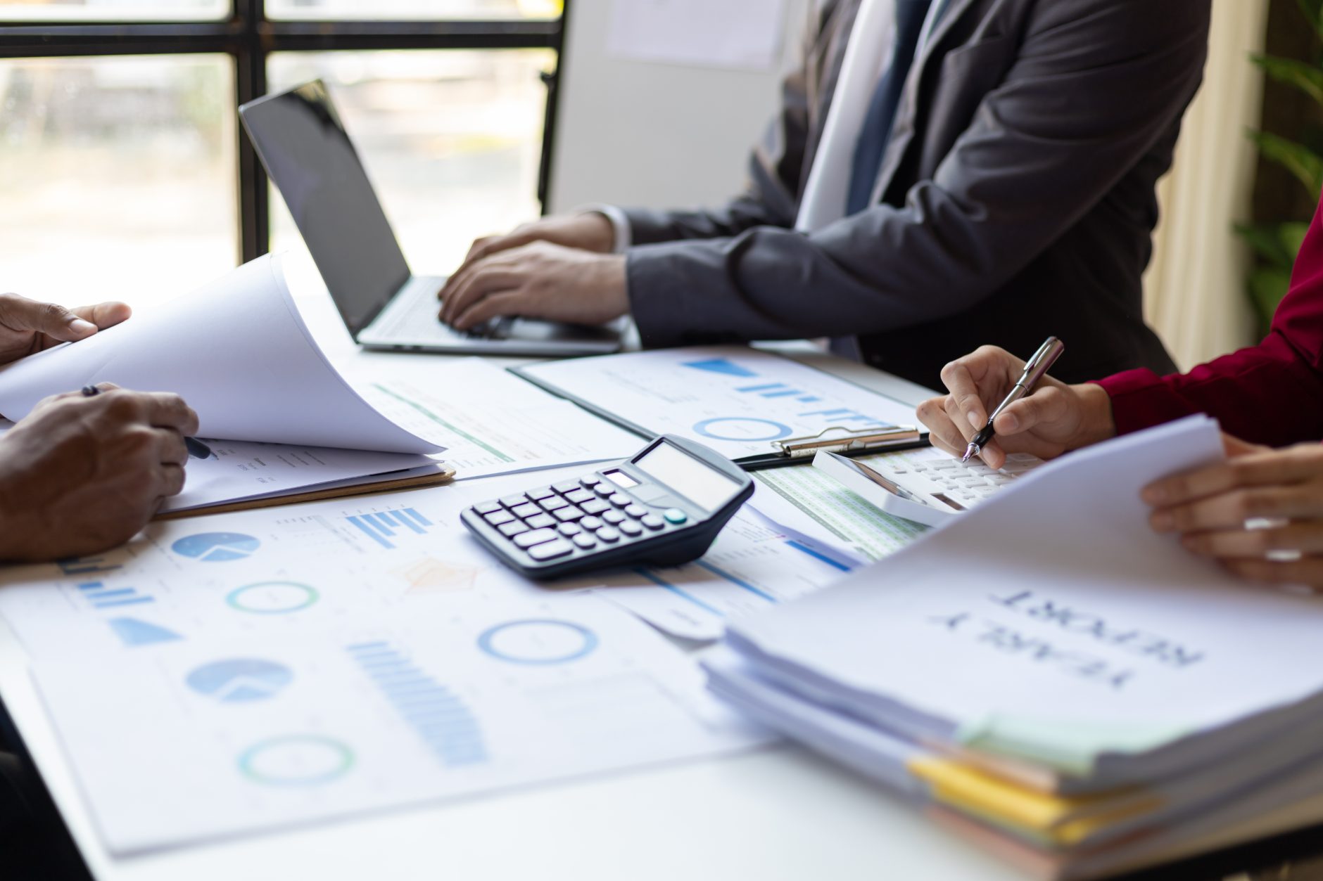 A finance team at a desk reviewing printed charts and a yearly report beside a laptop and calculator